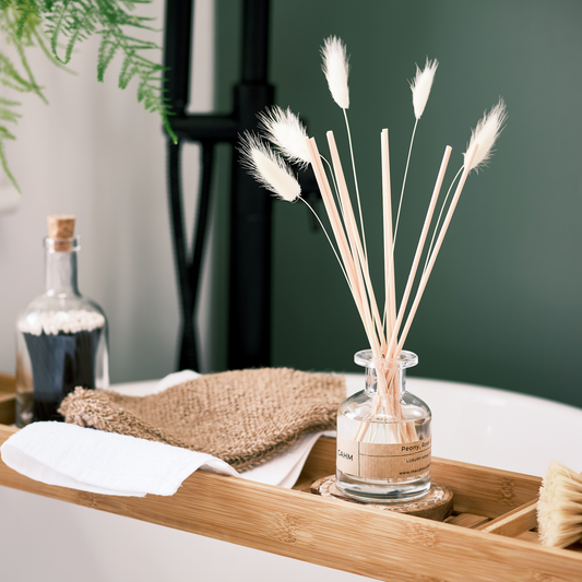 Reed diffuser in a glass bottle with decorative sticks on a wooden tray.