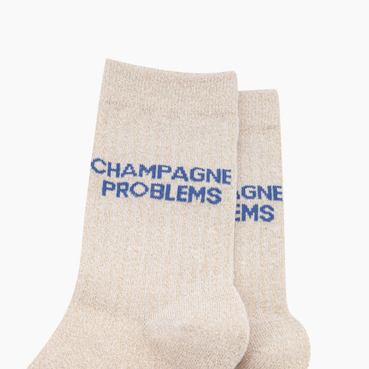Beige socks with blue text 'CHAMPAGNE PROBLEMS' on a white background