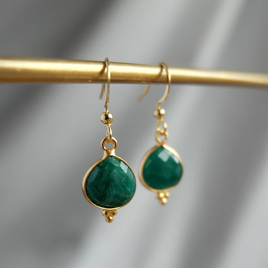 Gold earrings with green gemstones on a gold rod against a gray background