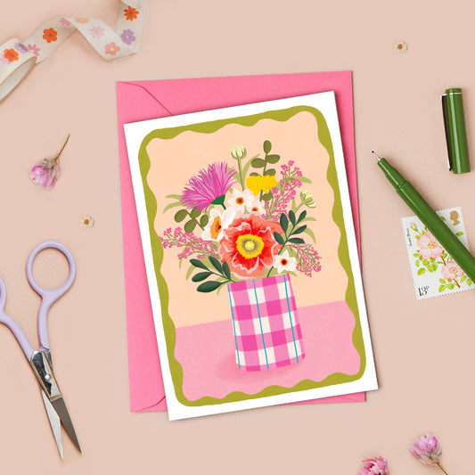 Floral card with pink envelope on a beige background with stationery items.