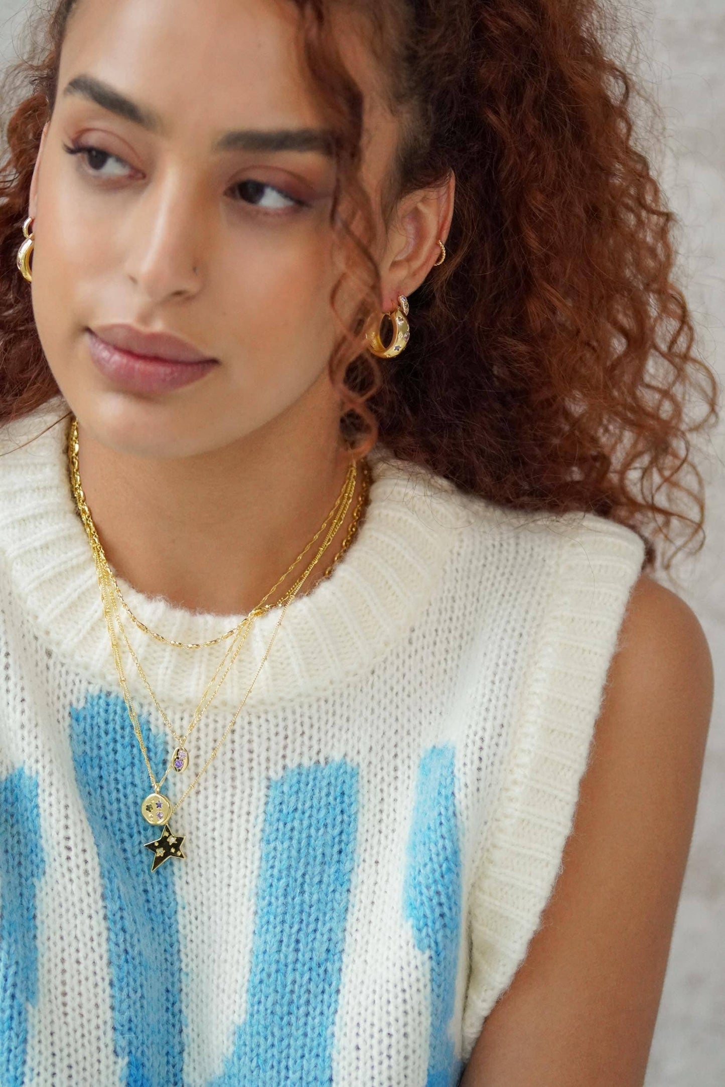 Woman wearing a white and blue patterned sleeveless sweater with gold jewelry.