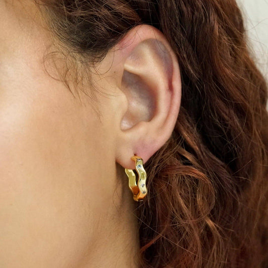 Close-up of an ear wearing a gold hoop earring with a blurred background