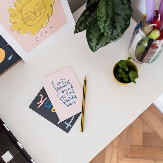 Desk with greeting cards, a pen, and small plants on a light surface.