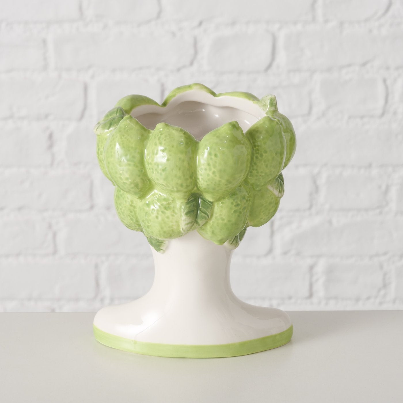 Decorative vase shaped like a cluster of green limes on a white pedestal against a textured white background.