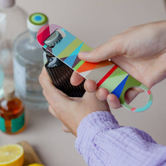 Person using a colorful bottle opener on a kitchen counter with bottles and lemons in the background.
