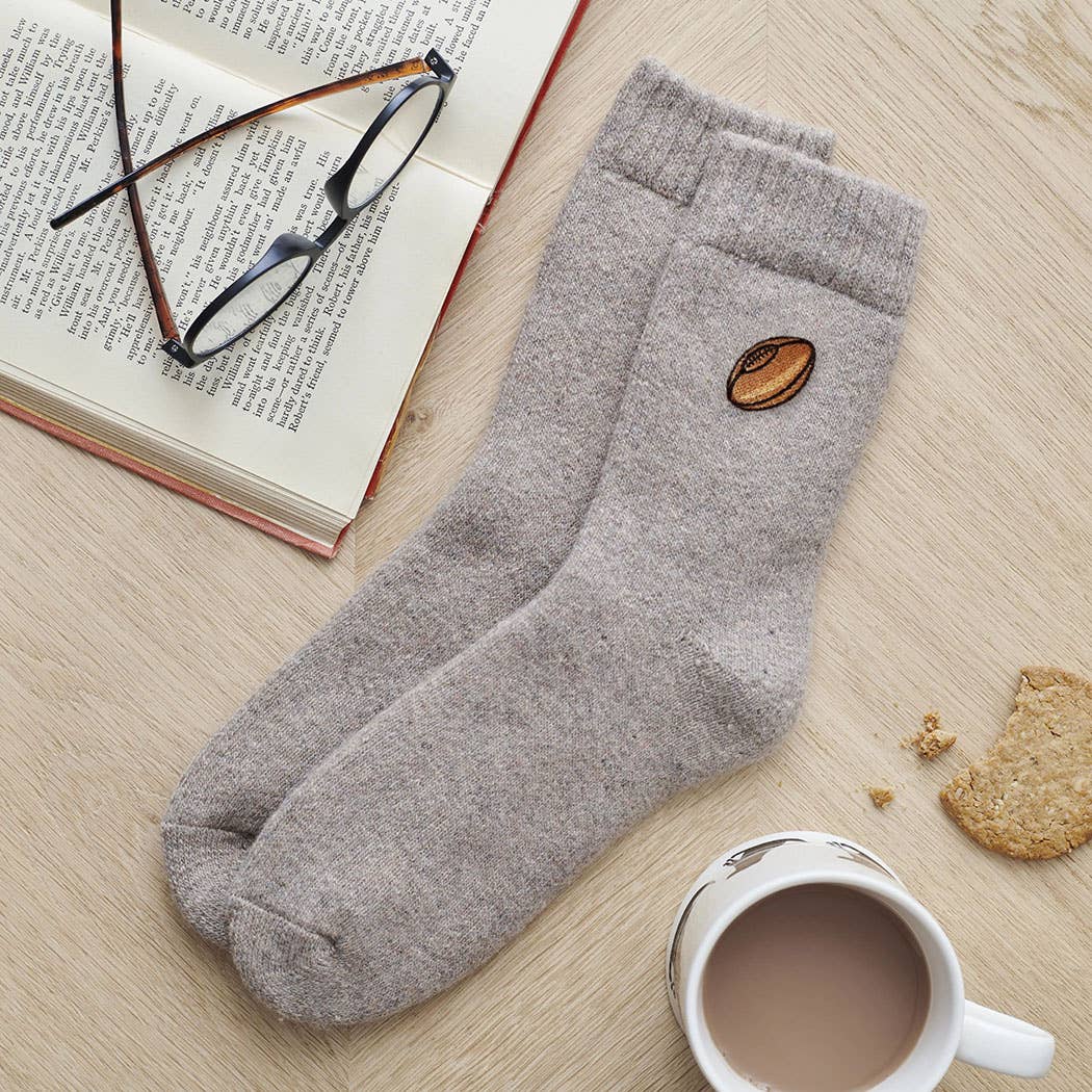 Gray socks with a coffee bean design on a wooden surface with a book, glasses, and cookies.