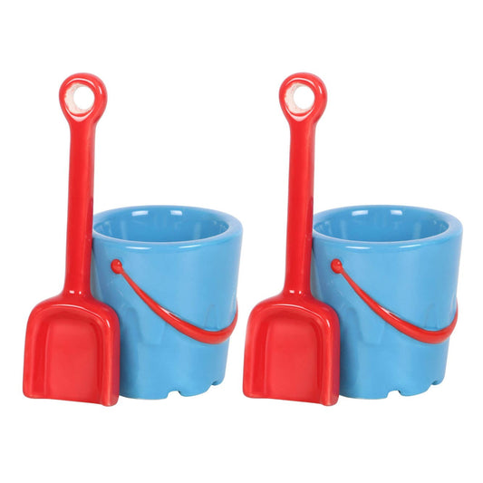 Two eggs in blue sand pails with red shovels on a beach.
