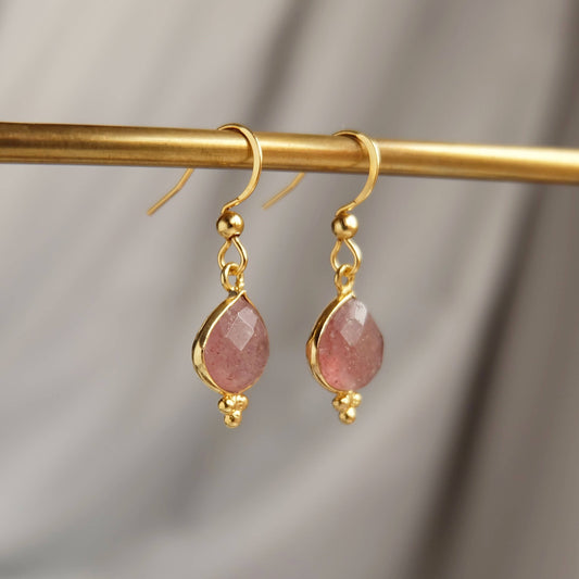 Gold earrings with pink stones on a gold rod against a gray background