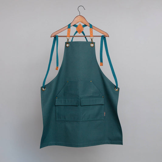 Green apron with teal straps hanging on a wooden hanger against a gray background