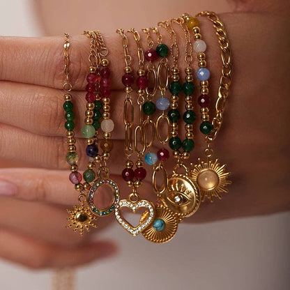 Multiple gold bracelets with various charms on a wrist against a neutral background