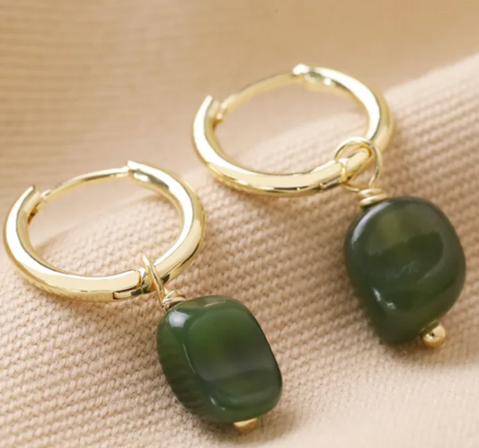 Gold hoop earrings with green beads on a beige fabric background