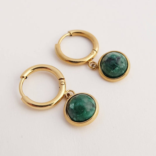 Gold hoop earrings with green gemstones on a light gray background