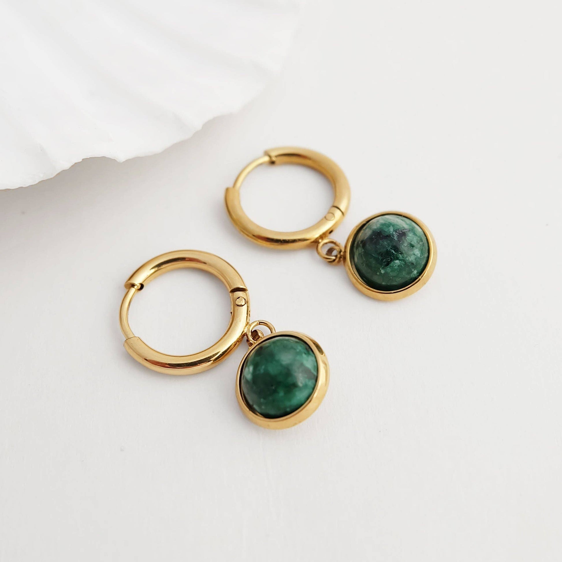 Gold hoop earrings with green gemstones on a white background