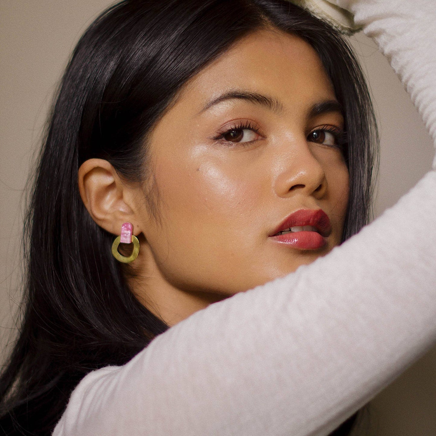 Woman with dark hair and red lipstick wearing earrings, with a neutral background