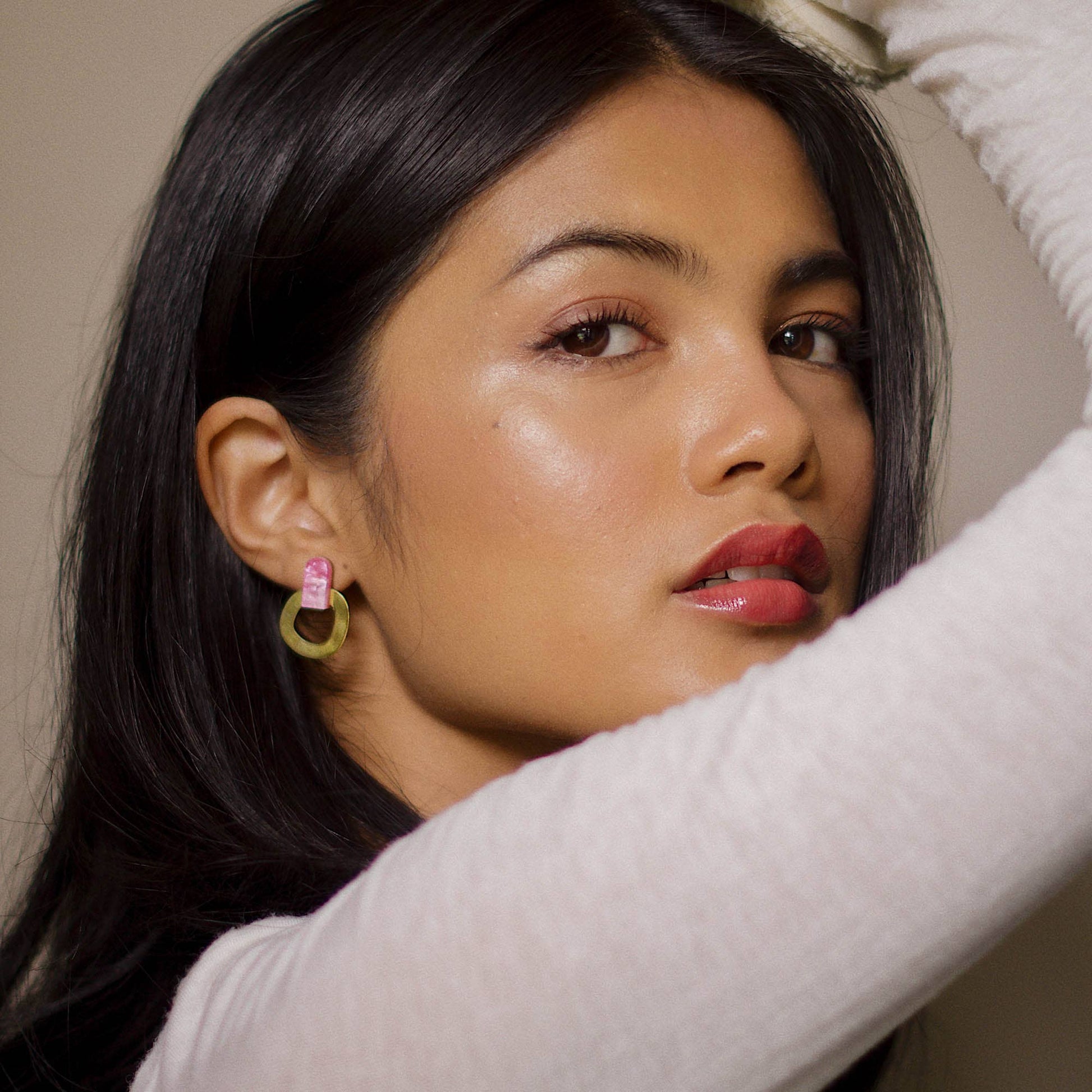 Woman with dark hair and red lipstick wearing earrings, with a neutral background
