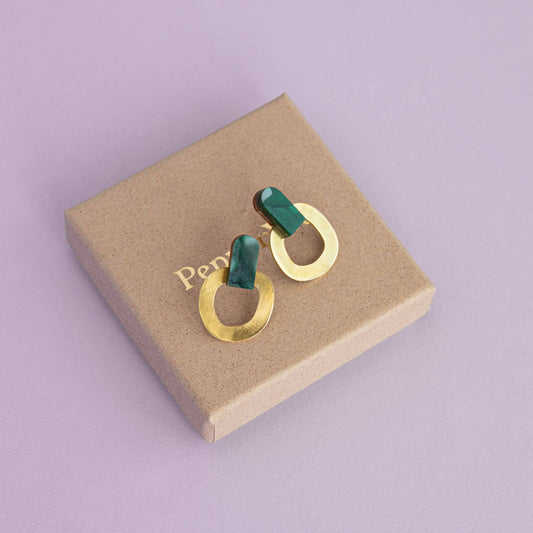 Gold and green earrings on a brown jewelry box with 'Pepper You' branding on a purple background.