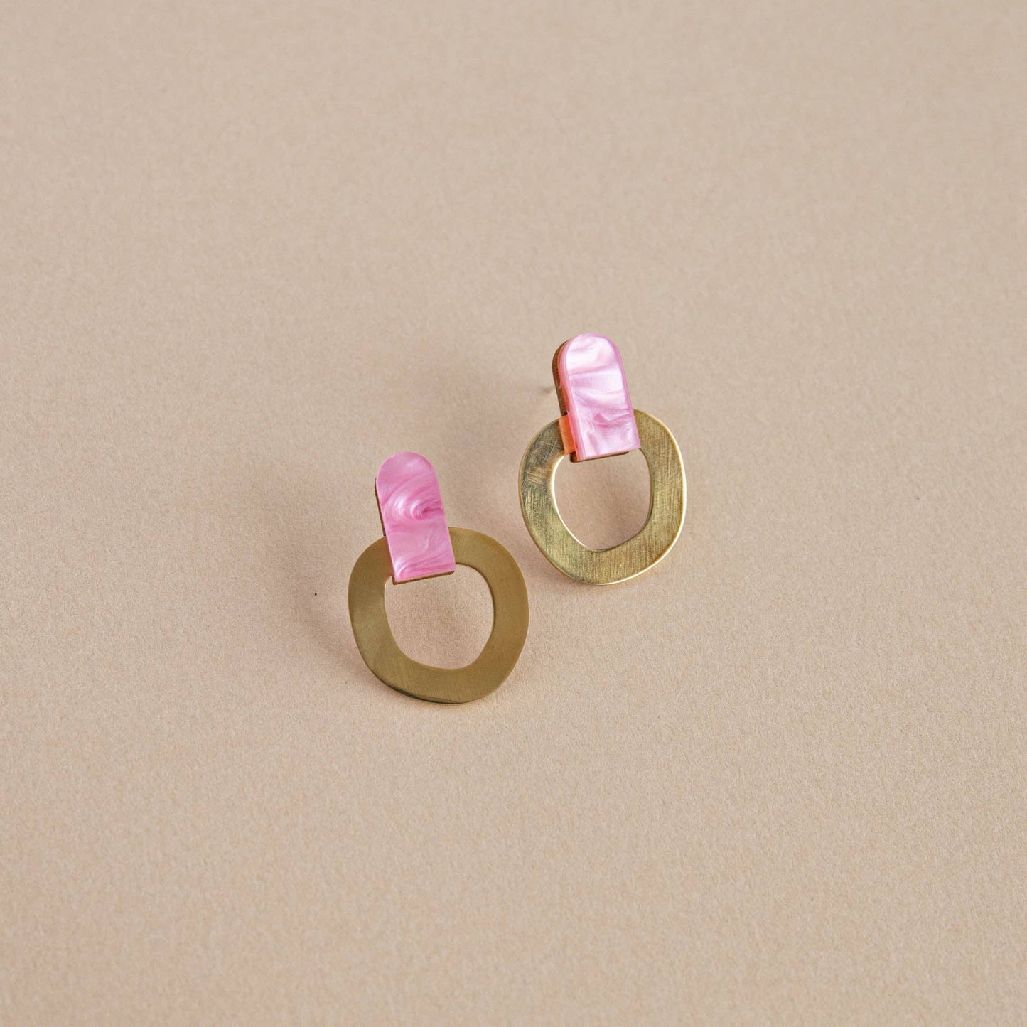 Pair of gold earrings with pink shell accents on a beige background