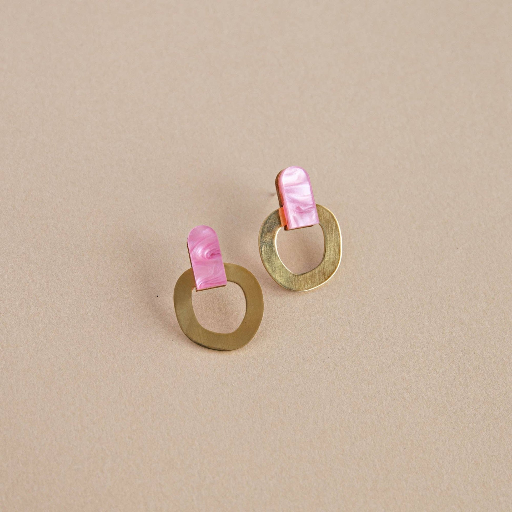 Pair of gold earrings with pink shell accents on a beige background