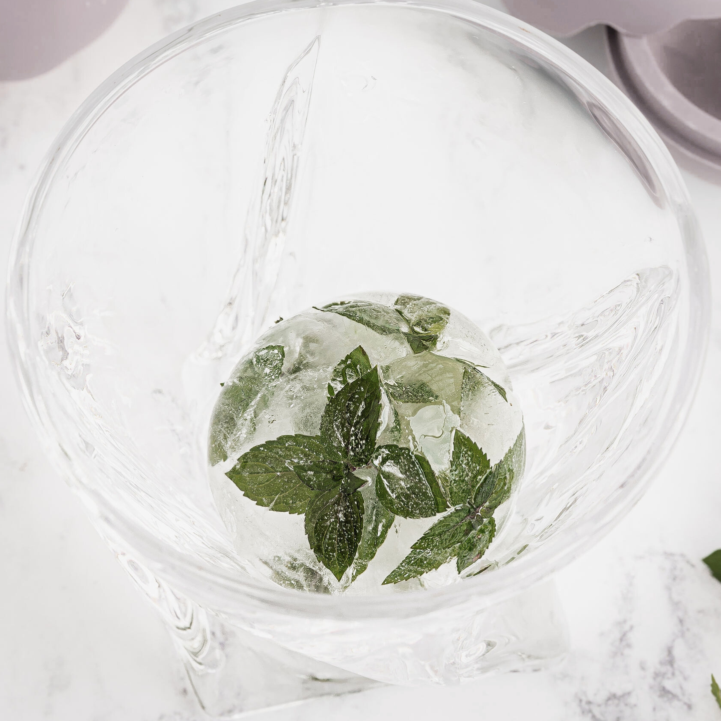 Clear glass with ice cubes and mint leaves on a marble surface