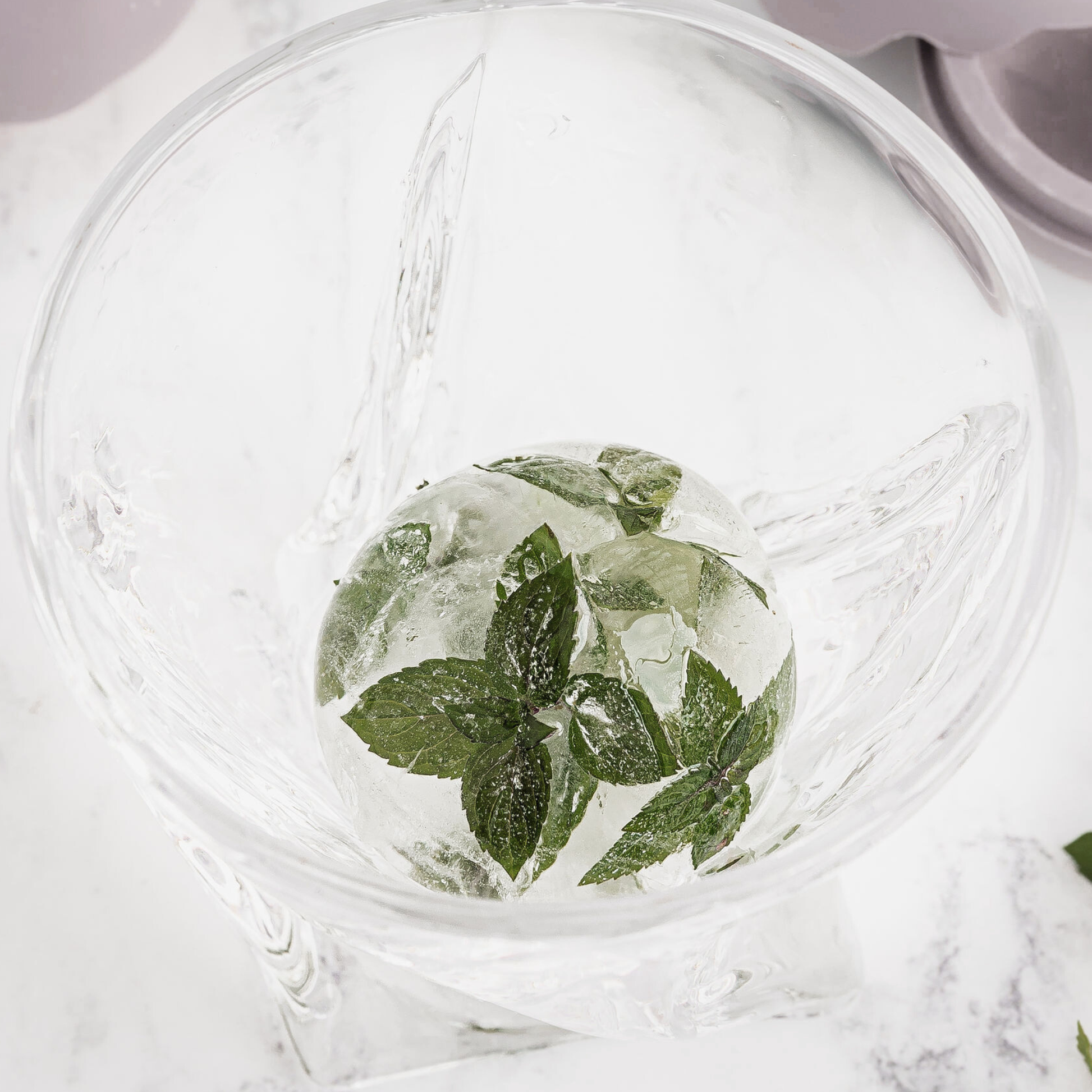 Clear glass with ice cubes and mint leaves on a marble surface