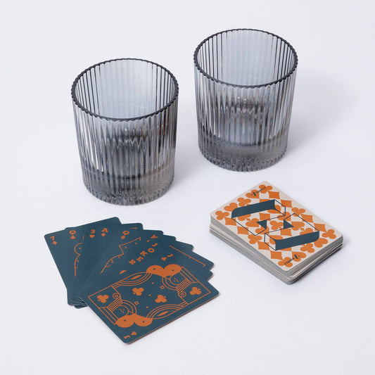 Two ribbed glass tumblers and a deck of playing cards on a white surface