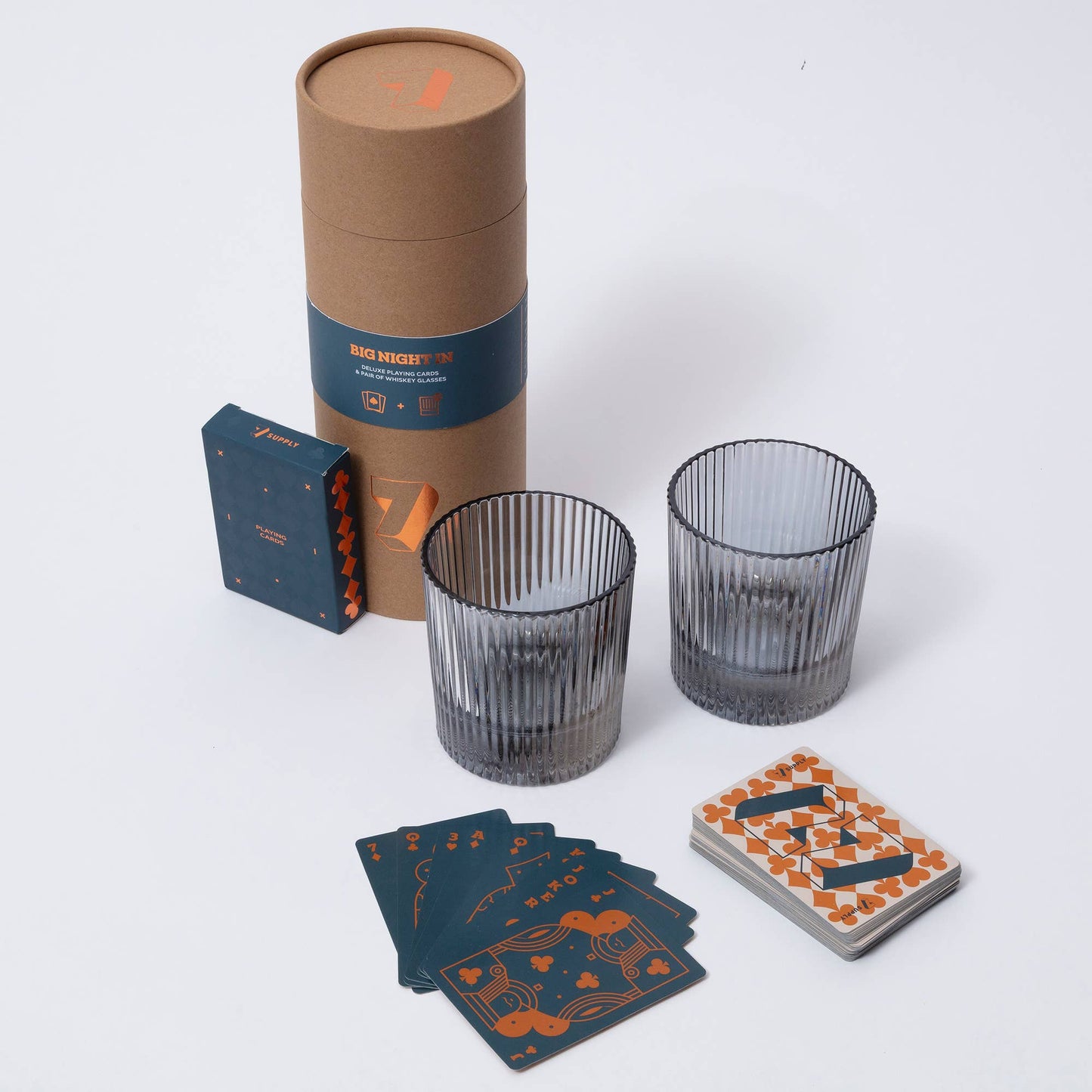 Two dark glass tumblers, a cardboard tube, and playing cards on a white background
