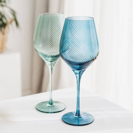 Two textured wine glasses, one blue and one green, on a white surface with a neutral background.
