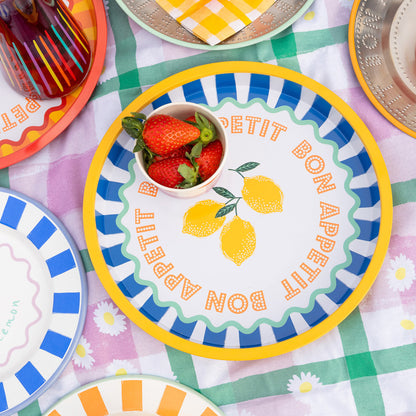 Colorful plates with 'Petit Bon Appetit' text and lemon design on a checkered tablecloth.