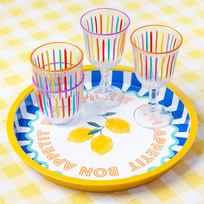 Colourful striped glasses on a decorative plate with lemon design on a checkered tablecloth.