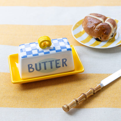 Butter dish with checkered lid on a yellow tray, next to a plate of pastries.