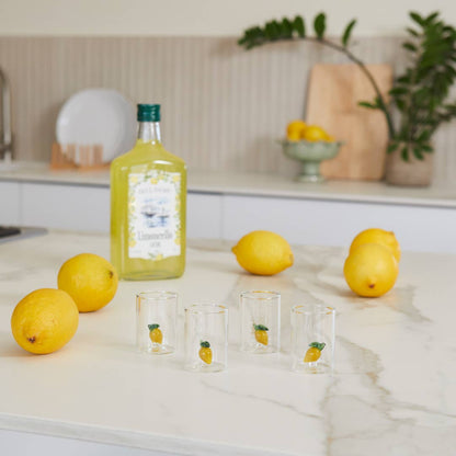 Lemons and a bottle of lemon juice on a kitchen counter with glasses featuring lemon designs.