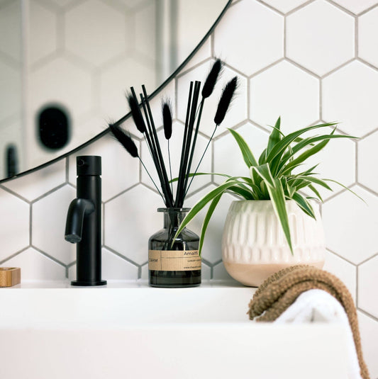 Decorative items including a black diffuser, vase with black feathers, and green plant against a hexagonal tile wall.