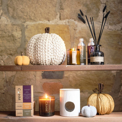 Candles and decorative items on a wooden shelf against a stone wall.
