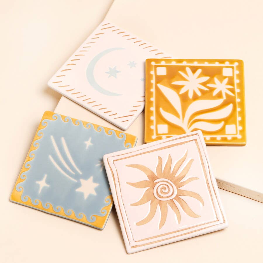 Four ceramic tiles with sun, moon, and star designs on a beige background