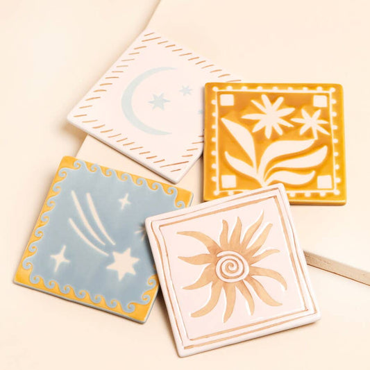 Four ceramic tiles with sun, moon, and star designs on a beige background