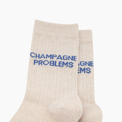 Beige socks with blue text 'CHAMPAGNE PROBLEMS' on a white background