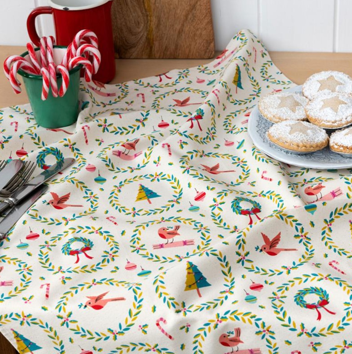 Tablecloth with festive design featuring birds and wreaths on a table with cookies and candy canes.