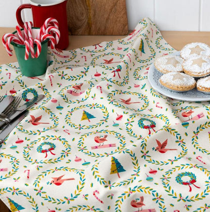 Tablecloth with festive design featuring birds and wreaths on a table with cookies and candy canes.