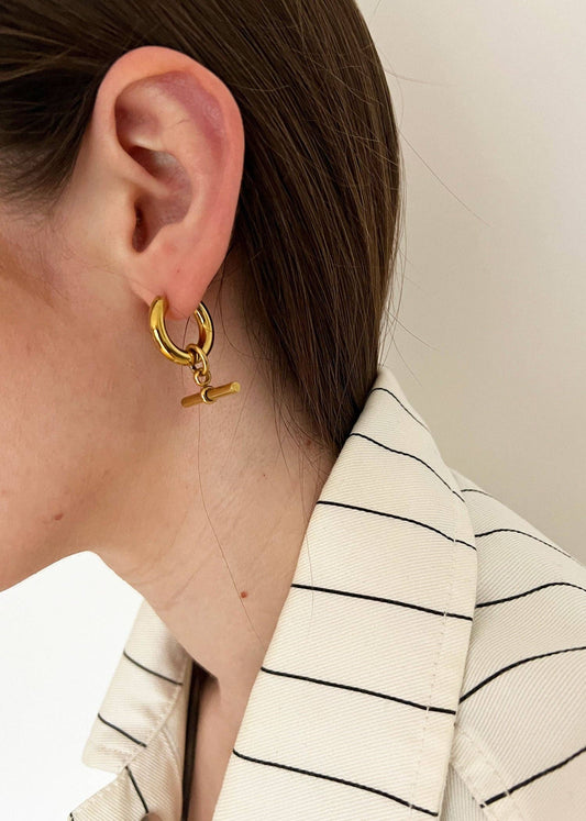 Close-up of a person wearing a gold earring with a small Nike logo.