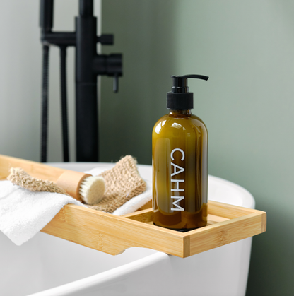 Brown bottle with pump labeled 'CAHM' on a wooden tray in a bathroom setting.