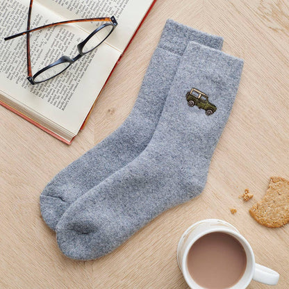 Gray socks with a car emblem on a wooden surface with a book, glasses, and a cup of coffee.