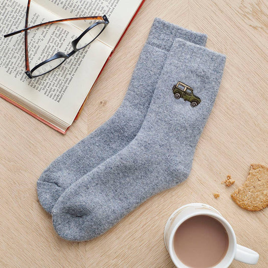 Gray socks with a car emblem on a wooden surface with a book, glasses, and a cup of coffee.