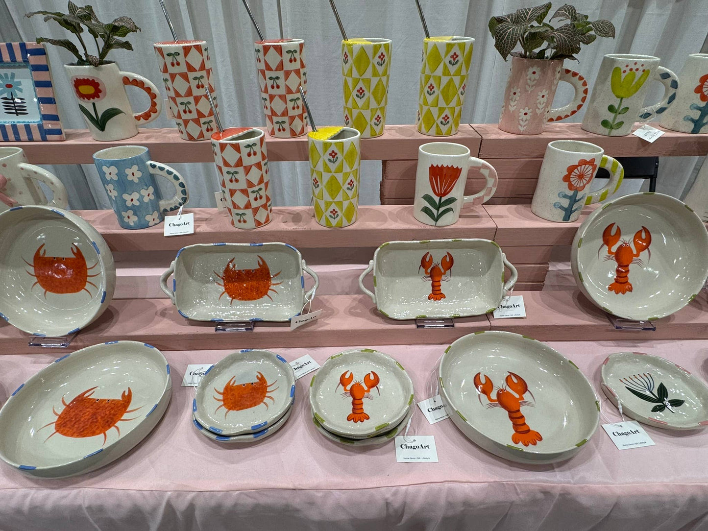 Collection of ceramic plates and mugs with animal designs on a pink tablecloth.