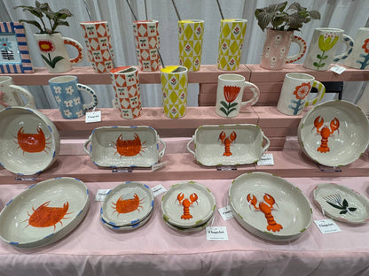 Collection of ceramic plates and mugs with animal designs on a pink tablecloth.