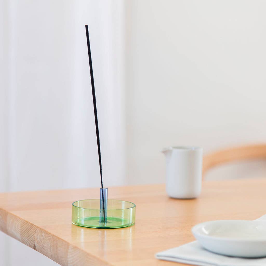 Incense stick in a green holder on a wooden table with a white background