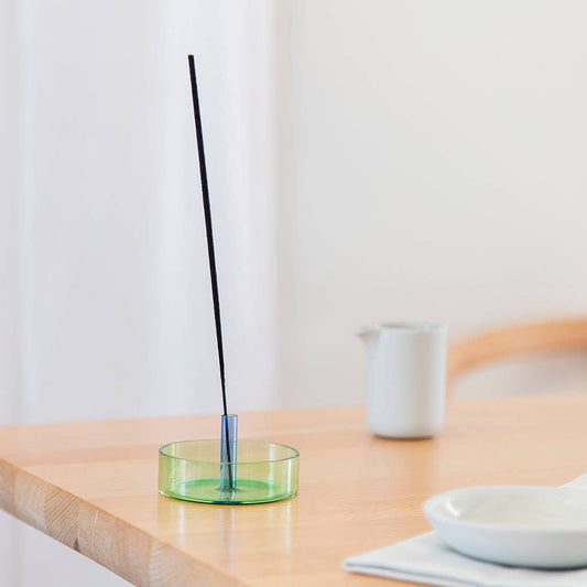Incense stick in a green holder on a wooden table with a white background