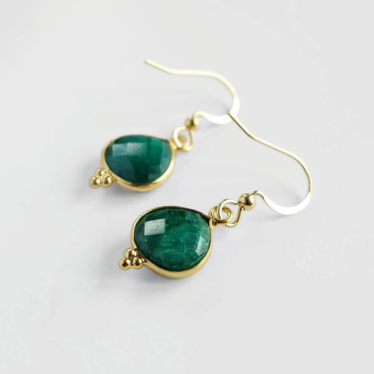Gold earrings with green gemstones on a light gray background