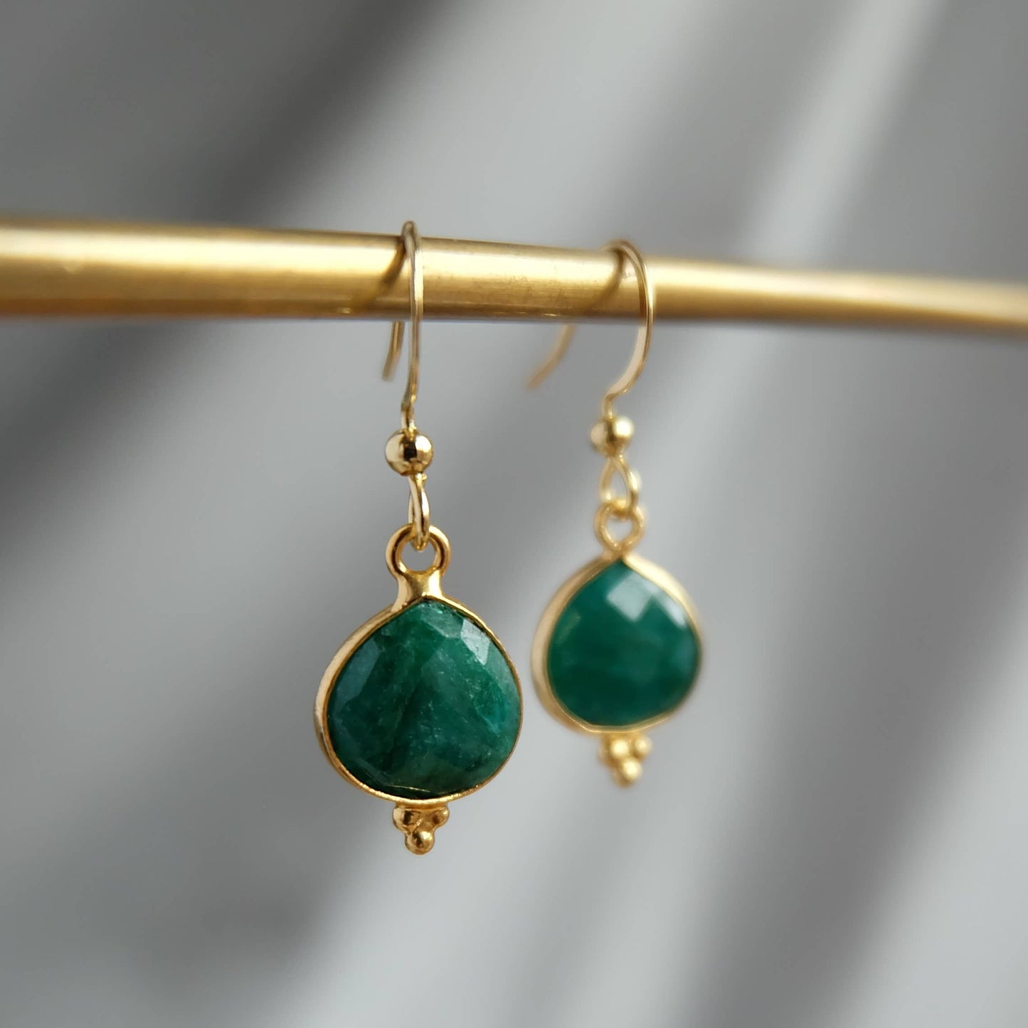 Gold earrings with green gemstones on a gold rod against a gray background