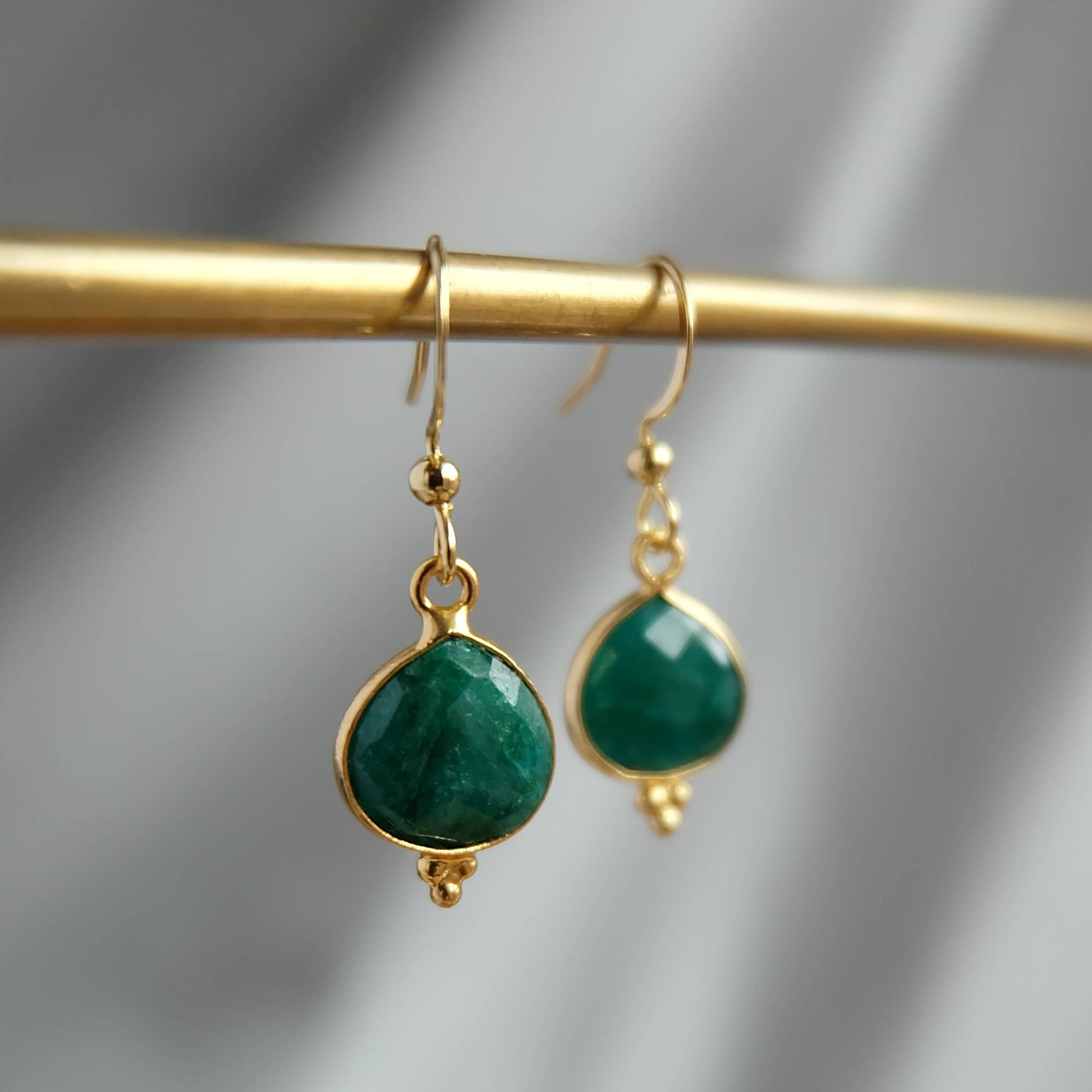 Gold earrings with green gemstones on a gold rod against a gray background