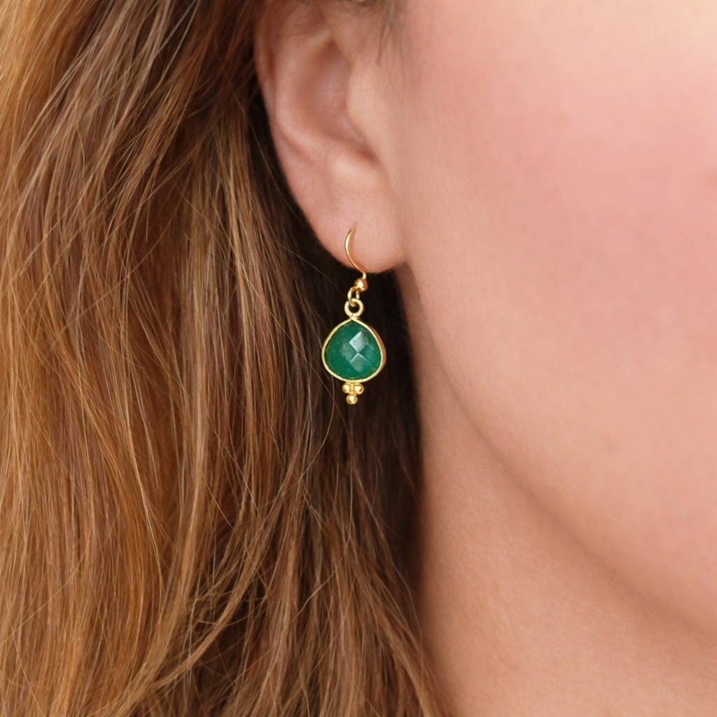 Gold earrings with green gemstones worn by a person with brown hair.